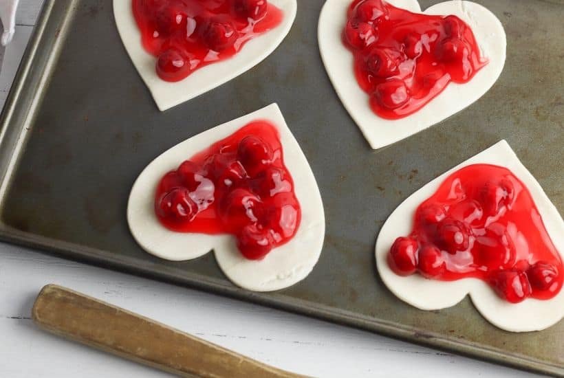 These Heart-Shaped Cherry Hand Pies are the perfect snack. Each hand pie is filled with sweet cherry pie filling sandwiched in between a flaky pie crust, then baked to perfection.