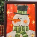 Decorate your home for the holiday season with this easy-to-make Lighted Snowman Picture. It’s fun to put together and perfect for hanging up around the home to get into the holiday spirit. This DIY Christmas craft is made with a gift bag and a dollar store frame. It is a fun dollar store Christmas craft.