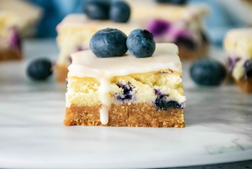 Ditch the traditional cheesecake that you have to eat with a fork and try this simple recipe for Blueberry Cheesecake Bars. These moist and delicious bars are full of sweet flavor and are perfect for a grab and go dessert. This easy blueberry dessert is a perfect dessert recipe for a party or potluck. Make this delicious bar recipe while blueberries are in peak season during the summer months.